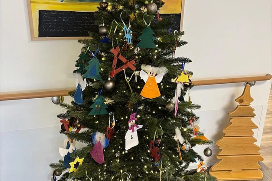 Weihnachtsbaum mit selbstgebastelten Anhängern aus Filz und Papier, darunter Engel, Sterne und Tannenbäume, vor einem Gemälde an der Wand.