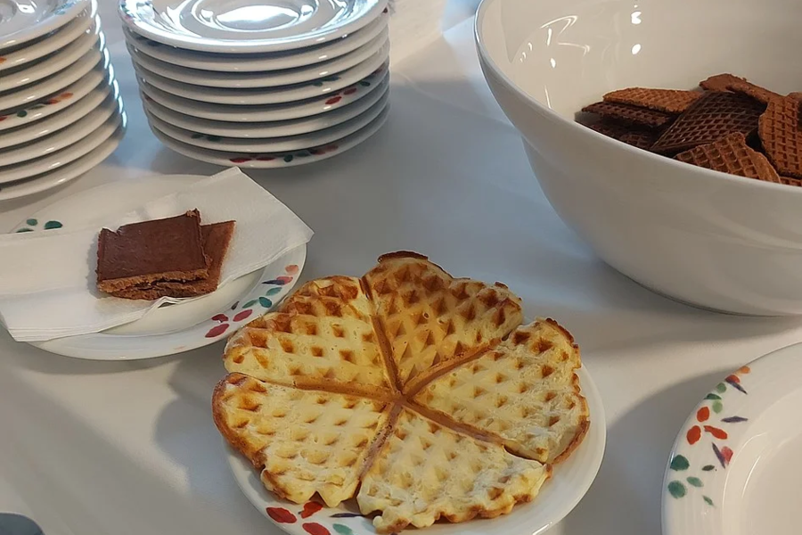 Auf einem Tisch liegen ein Teller mit einem herzförmigen Waffelkreis, ein Teller mit einem Schokoriegel, ein Stapel kleiner Teller und eine Schüssel mit Waffelstücken.