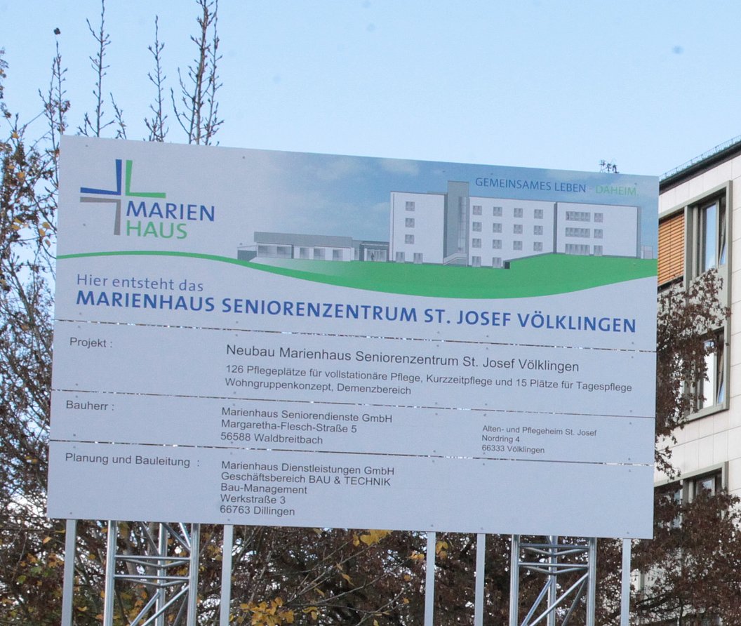 Bauschild mit Informationen zum Neubau des Marienhaus Seniorenzentrums St. Josef Völklingen vor Bäumen und klarem Himmel