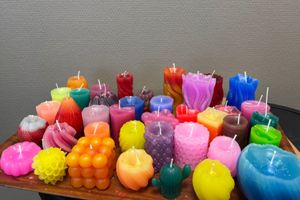 Verschiedene bunte Kerzen in unterschiedlichen Formen und Größen auf einem Holztisch vor grauer Wand